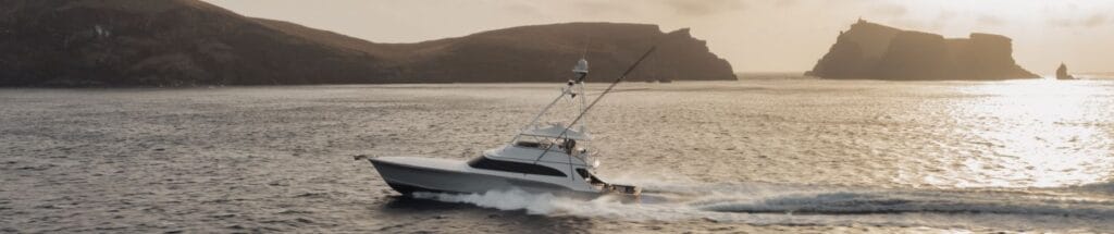 Motorjacht bei Sonnenuntergang vor felsiger Küste